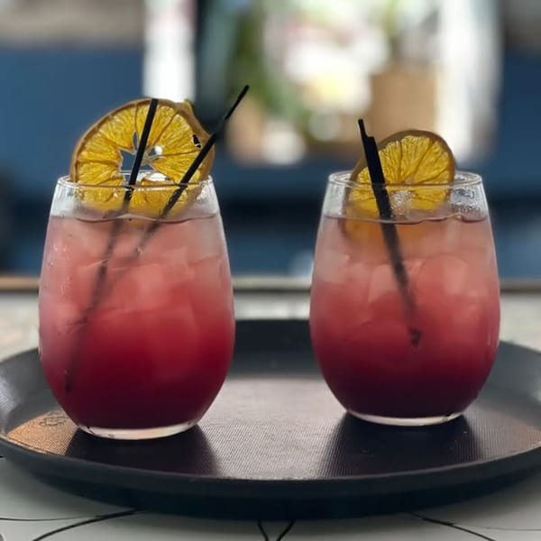 Two red cocktails with dried orange slices and black straws on a dark tray.