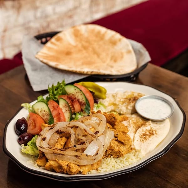 A Mediterranean chicken shawarma platter with rice, hummus, salad, and pita bread.