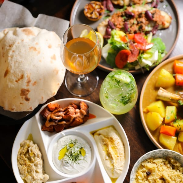 A table laden with Mediterranean dishes including pita, hummus, baba ghanoush, and a stew.
