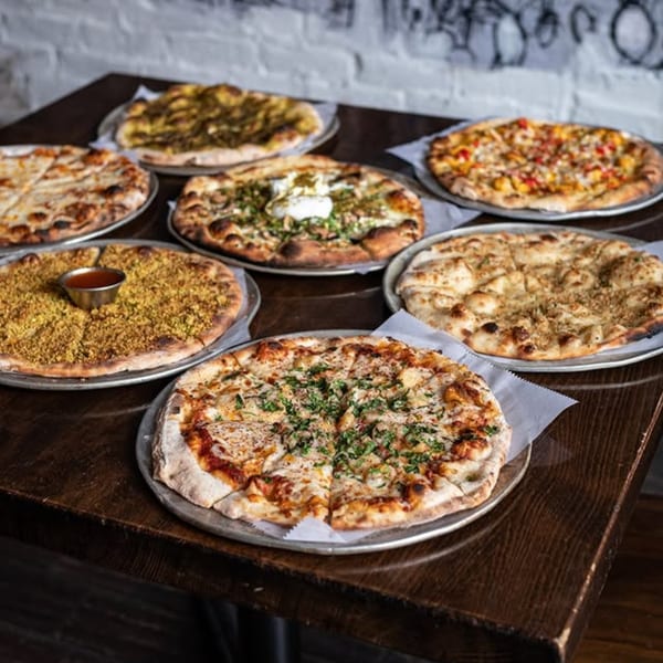 A wooden table laden with seven different Mediterranean pizzas, including za'atar and cheese varieties.