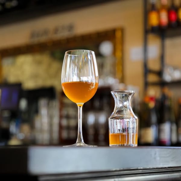 A glass of amber liquid and a small carafe on a dark bar counter at Dar525.