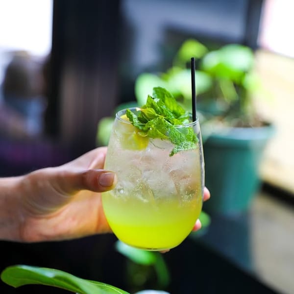 Hand holding a refreshing Dar525 Mediterranean lime and mint cocktail with ice and a straw.