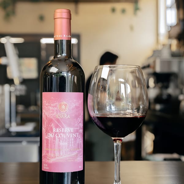 A bottle of Chateau Ksara red wine and a glass of red wine on a wooden table.