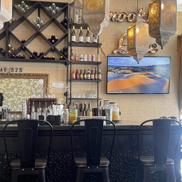 A Mediterranean restaurant bar with wine racks, shelves of bottles, and decorative lanterns above.
