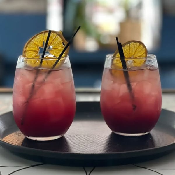Two red cocktails with dried orange slices and black straws on a dark tray at Dar525.