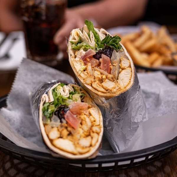 Two chicken shawarma wraps, cut in half, with lettuce, tomatoes, and onions, served in a basket.