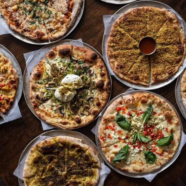 An overhead view of six different Mediterranean pizzas on metal trays, some with dips.
