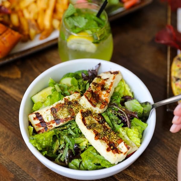 A Mediterranean salad with grilled halloumi cheese, mixed greens, and cucumber, next to a mojito.