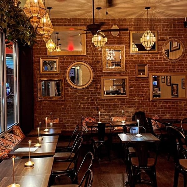 Cozy Mediterranean restaurant interior with brick walls, ornate lanterns, mirrors, and set tables.