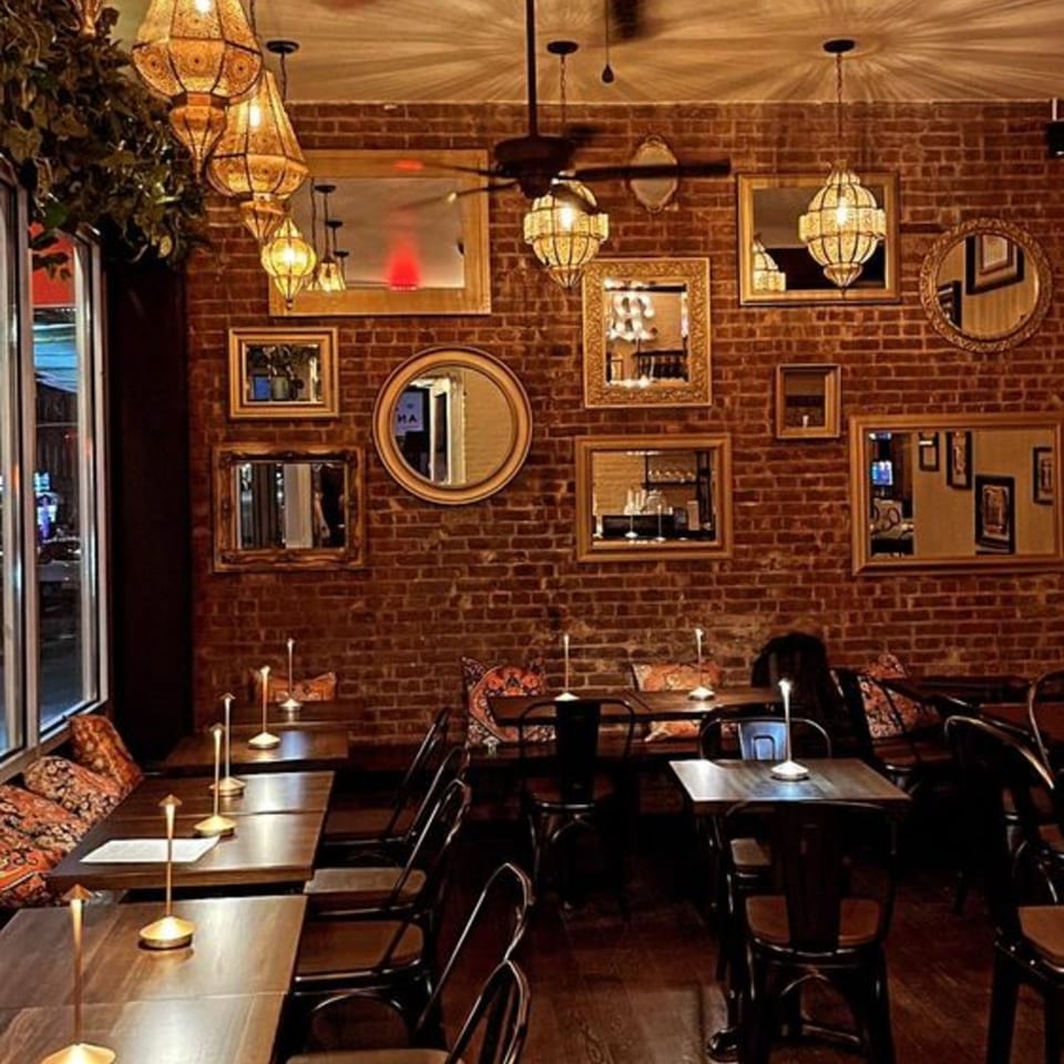 Cozy Mediterranean restaurant interior with brick walls, ornate lanterns, mirrors, and set tables.