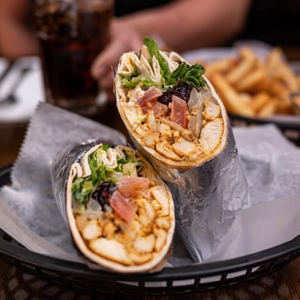 Two chicken shawarma wraps with lettuce, tomatoes, and onions, served in a basket with fries.
