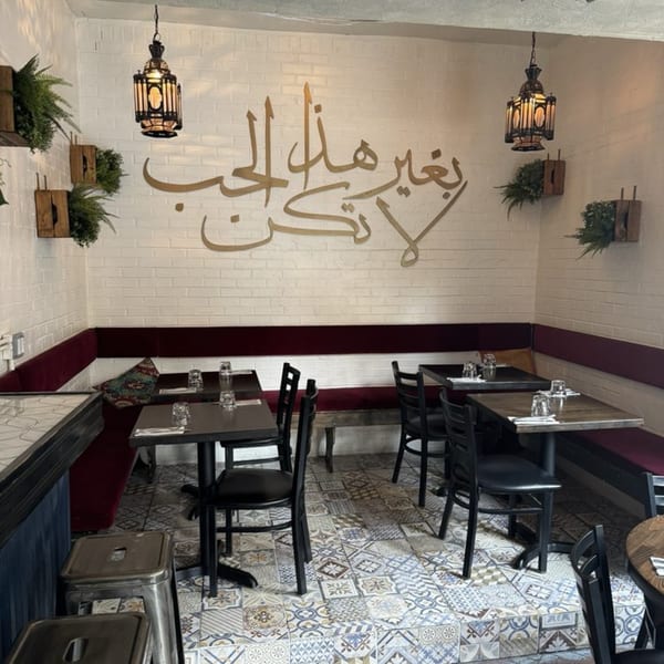 Interior of Dar525, featuring white brick walls with Arabic calligraphy, red banquettes, and patterned floor tiles.