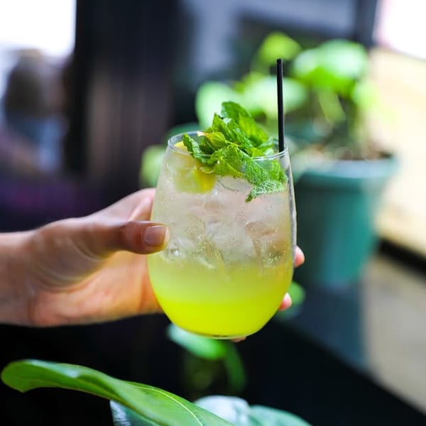 A hand holds a refreshing Dar525 Mediterranean lime and mint drink with ice and a black straw.