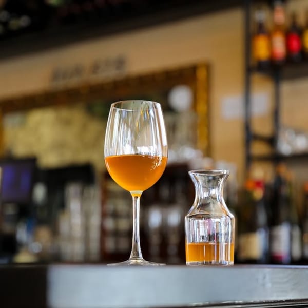 A wine glass and a small carafe filled with amber liquid on a bar top at Dar525.