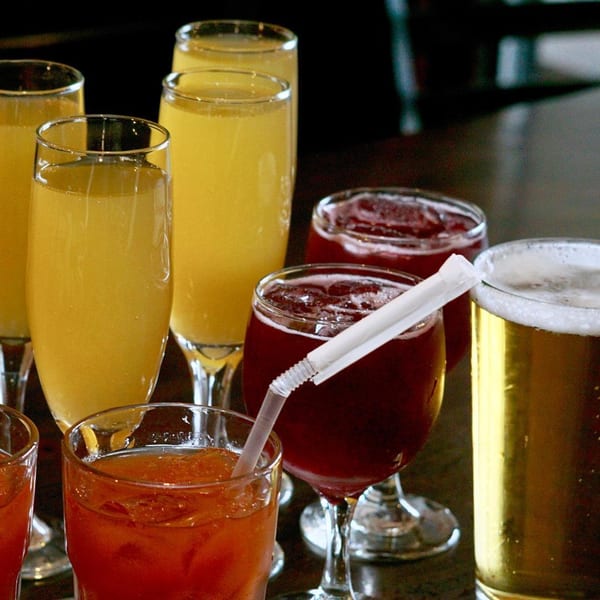 Assortment of drinks including mimosas, red cocktails, and beer on a dark table at Dar525.