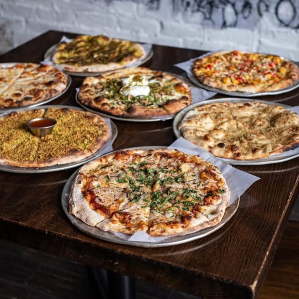 Seven Mediterranean pizzas with various toppings, including za'atar and cheese, arranged on a wooden table.