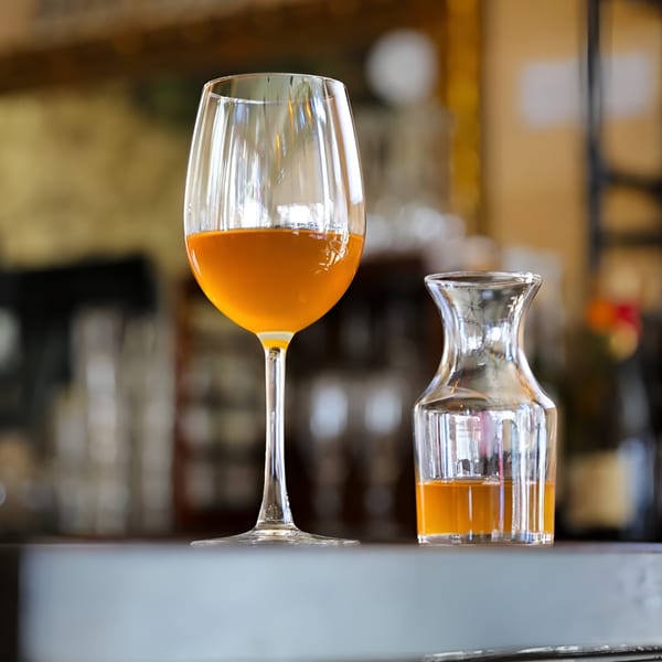 A glass of amber liquid next to a small carafe with more of the same drink.